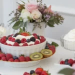 A dessert table with a centerpiece of berries and cream, fresh fruits, and decorative flowers.