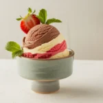 Neapolitan ice cream scoop featuring chocolate, vanilla, and strawberry layers in a modern white bowl with a mint garnish."