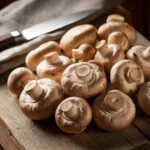 Fresh cremini mushrooms on a wooden cutting board with a knife and napkin.